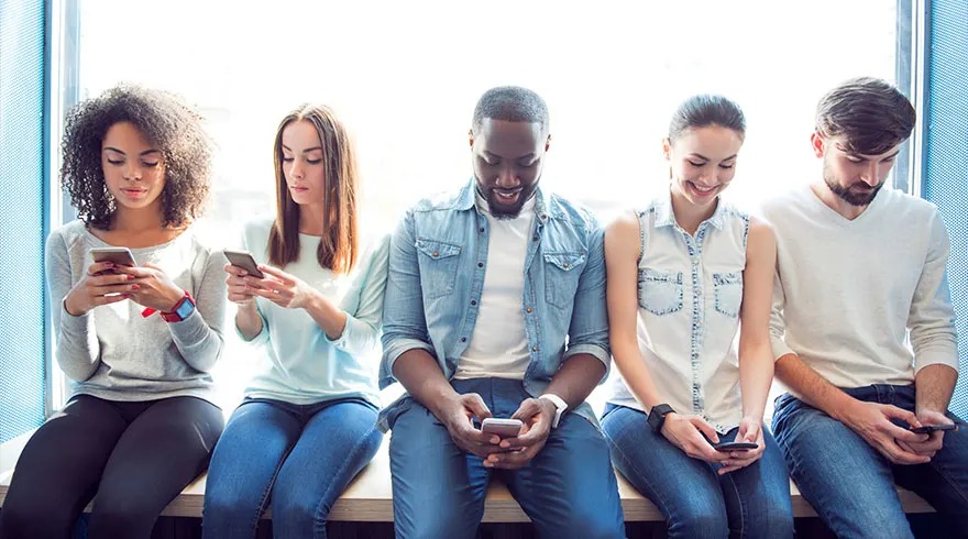 Cinq personnes assises près d'une fenêtre bleue, utilisant des smartphones. Vêtements variés, jeans et hauts décontractés.