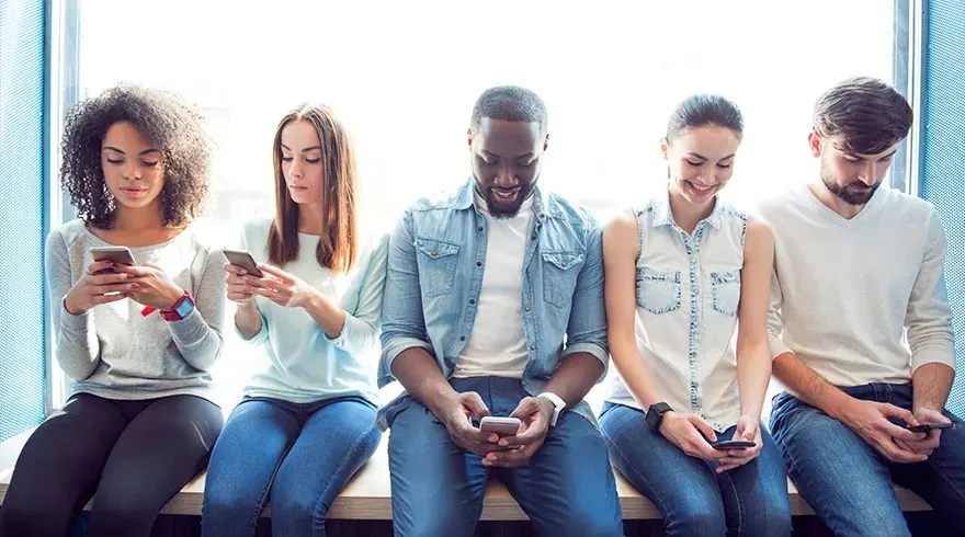 Cinq personnes assises près d'une fenêtre bleue, utilisant des smartphones. Vêtements variés, jeans et hauts décontractés.