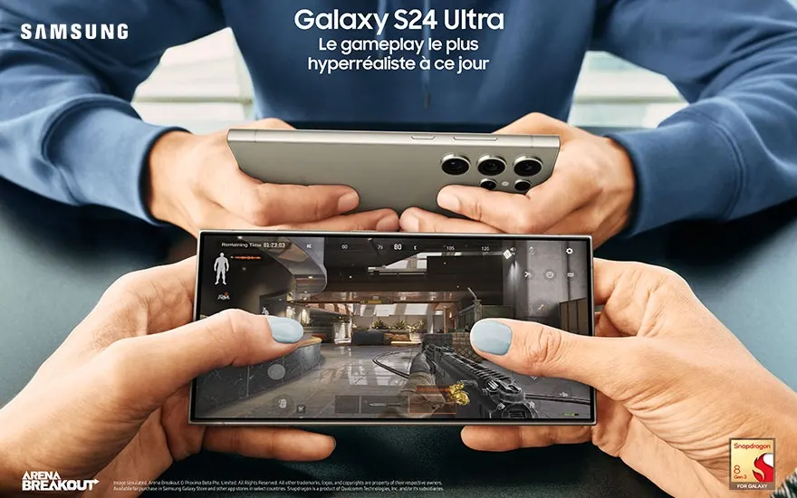 Deux smartphones Samsung Galaxy S24 Ultra sont tenus, l'un affichant un jeu vidéo de tir. Fond bleu.