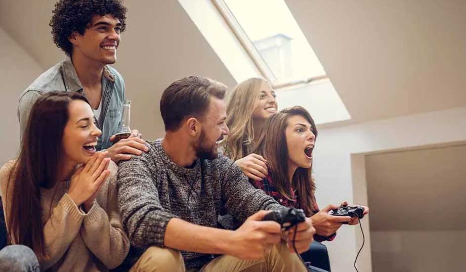 Vijf personen in een kamer, sommigen met gamecontrollers, tegen een achtergrond van een raam.