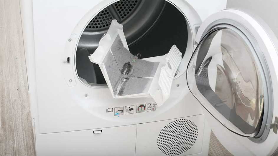 Een witte droogkast met open deur en een vol pluizenfilter. De filter is grijs door stof.