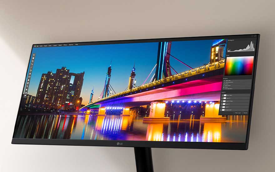 Un écran LG ultra-large montre une photo de nuit colorée d’un pont et de bâtiments, avec un logiciel d’édition ouvert dessus.