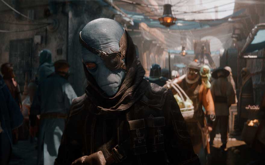 Dans une rue animée, un être bleu porte des lunettes et une cape sombre. Des lampes suspendues illuminent la scène.