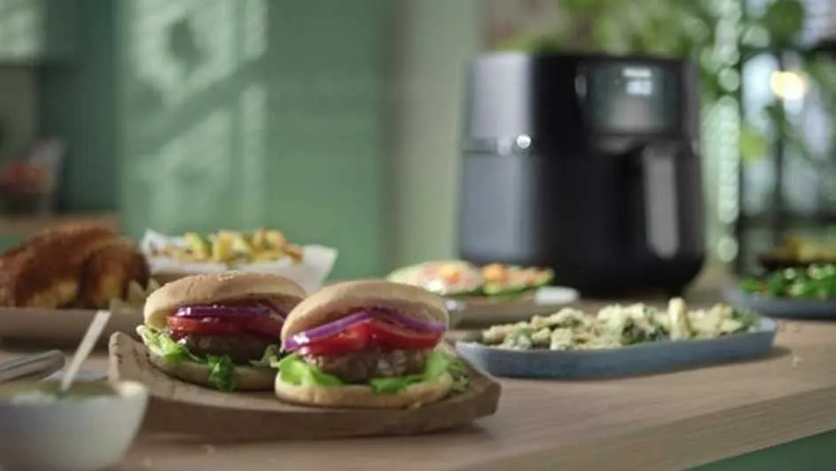 A table with burgers, salad, and an air fryer. The burgers have lettuce, tomato, and red onion.