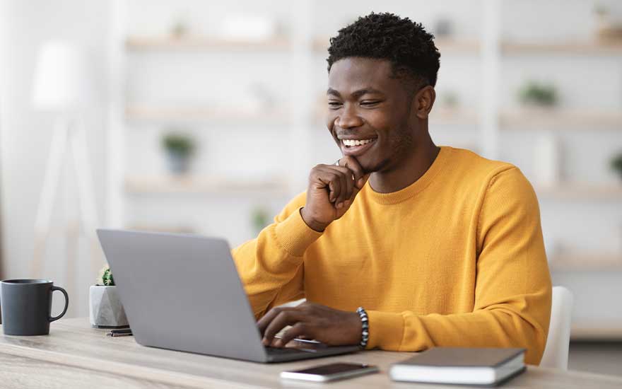 Bureau avec ordinateur portable gris, tasse noire, smartphone et plante. Étagères blanches en arrière-plan.
