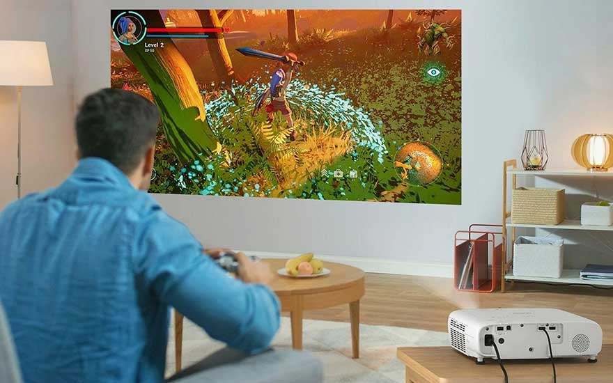 Un homme joue à un jeu vidéo avec une manette tandis qu’un projecteur affiche une grande image sur le mur du salon.