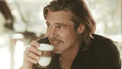 Een close-up van een persoon die een gelaagde drank in een helder glas vasthoudt tegen een vage achtergrond.