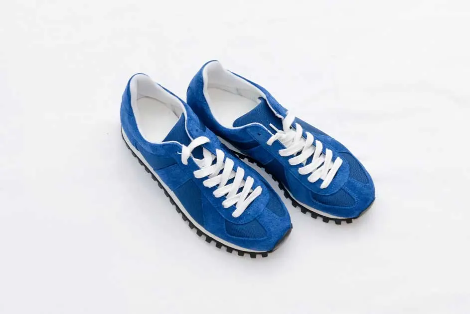 Twee blauwe sneakers met witte veters liggen op een witte achtergrond. De zolen hebben een zwart profiel.