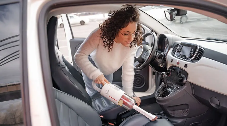 Interieur van een witte auto met zwart lederen stoelen, een stofzuiger op de voorstoel.