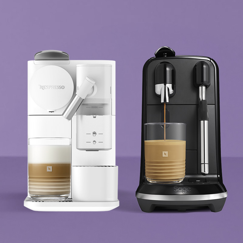 Une machine à café Nespresso blanche et une noire avec buse vapeur, chacune accompagnée d’une boisson lactée au café crémeuse dans un verre, sur fond violet.