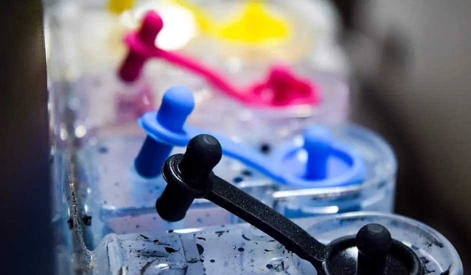 Een close-up van printerinktpatronen. Zwart, blauw, roze en geel zijn zichtbaar met plastic doppen en heldere containers.