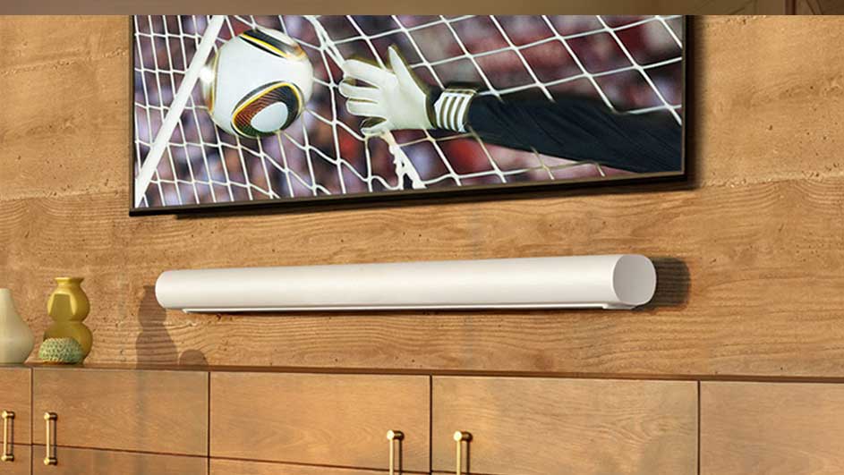Een tv aan een houten muur toont een voetbal die een net raakt, boven een witte soundbar en een houten kast.