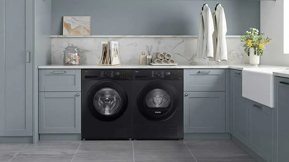 Een wasmachine en droger staan naast elkaar in een wasruimte met grijze kasten en accessoires.