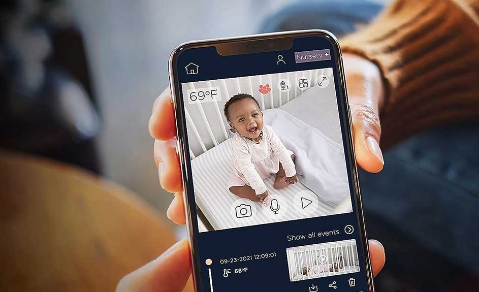 Een mobiele telefoon toont een baby in een wieg, via een app met temperatuur- en tijdinformatie.