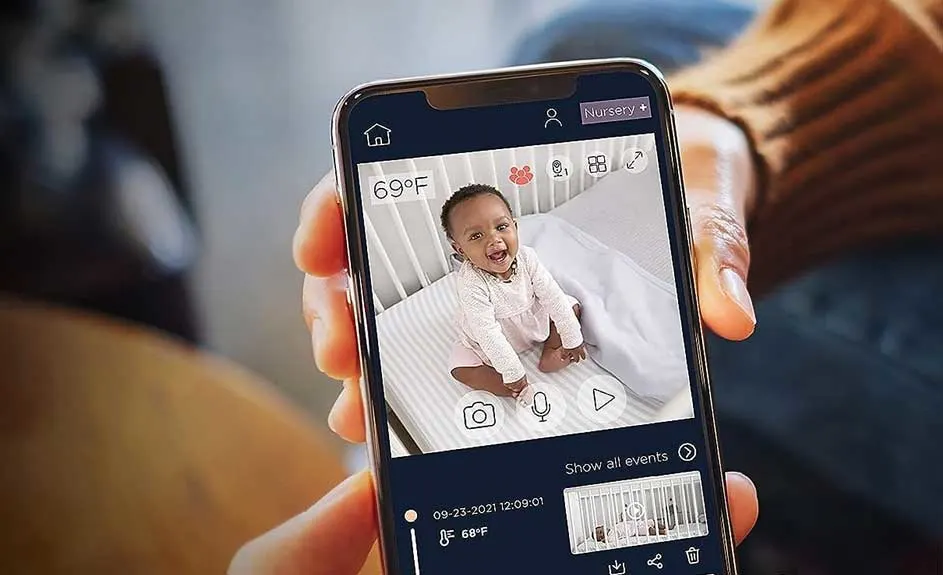 Een mobiele telefoon toont een baby in een wieg, via een app met temperatuur- en tijdinformatie.
