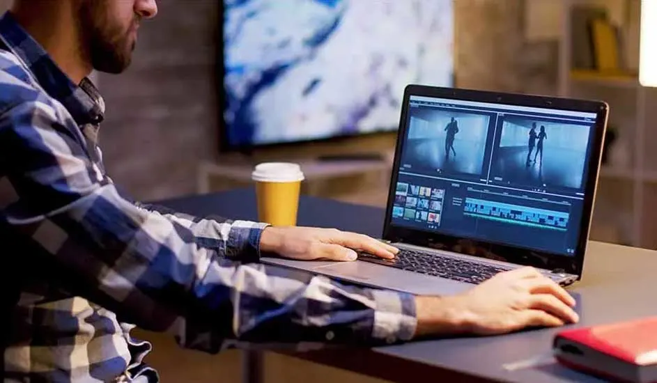 Een laptop toont videobewerkingssoftware naast een gele beker en een rode harde schijf op een bureau. Een tv staat op de achtergrond.