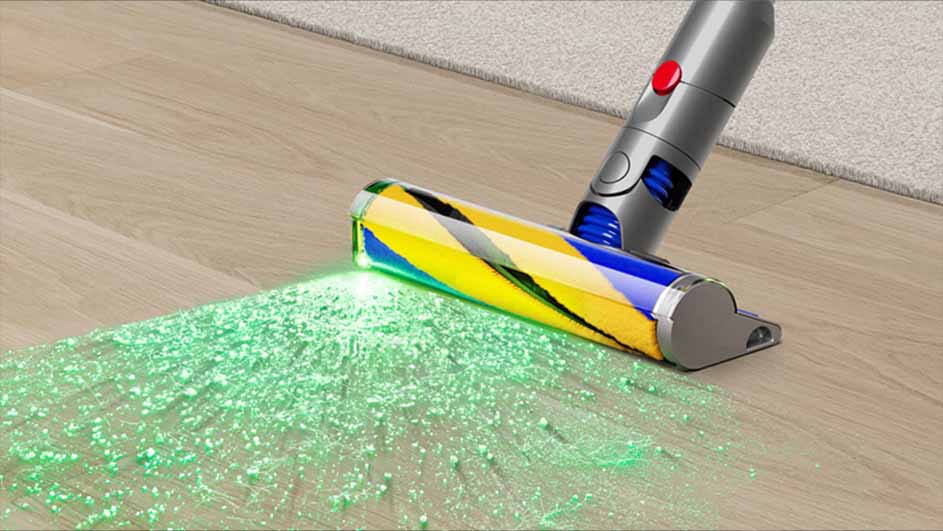 Un aspirateur gris et bleu avec une lumière verte nettoie un plancher en bois.