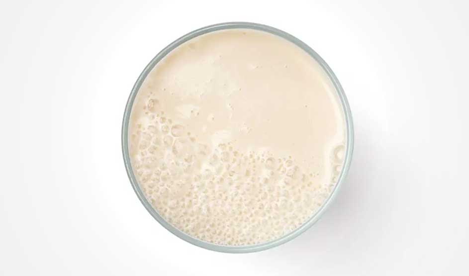 Vue aérienne d'un verre rempli d'un liquide beige mousseux sur un fond blanc.