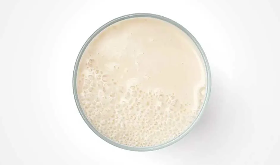 Vue aérienne d'un verre rempli d'un liquide beige mousseux sur un fond blanc.