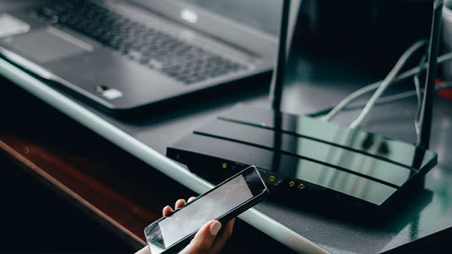 Ordinateur portable et routeur noir sur une surface, avec un smartphone tenu à la main au premier plan.