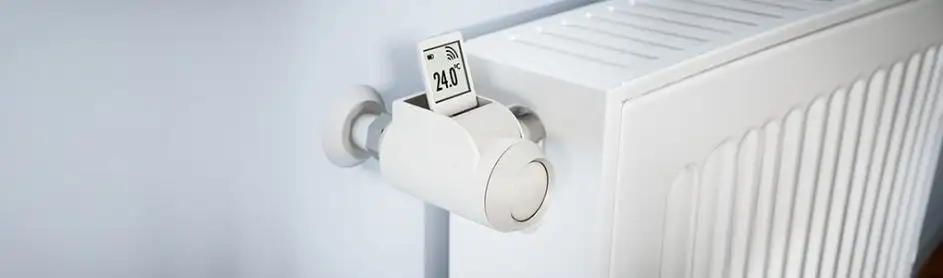Een witte radiator tegen een witte muur met een digitale thermostaat die 24.0 graden Celsius aangeeft.