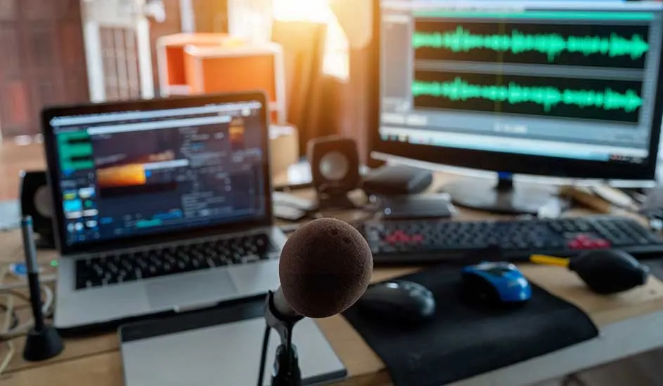 Een bureau met een laptop, een scherm met audiogolven, een microfoon, een toetsenbord en muizen.