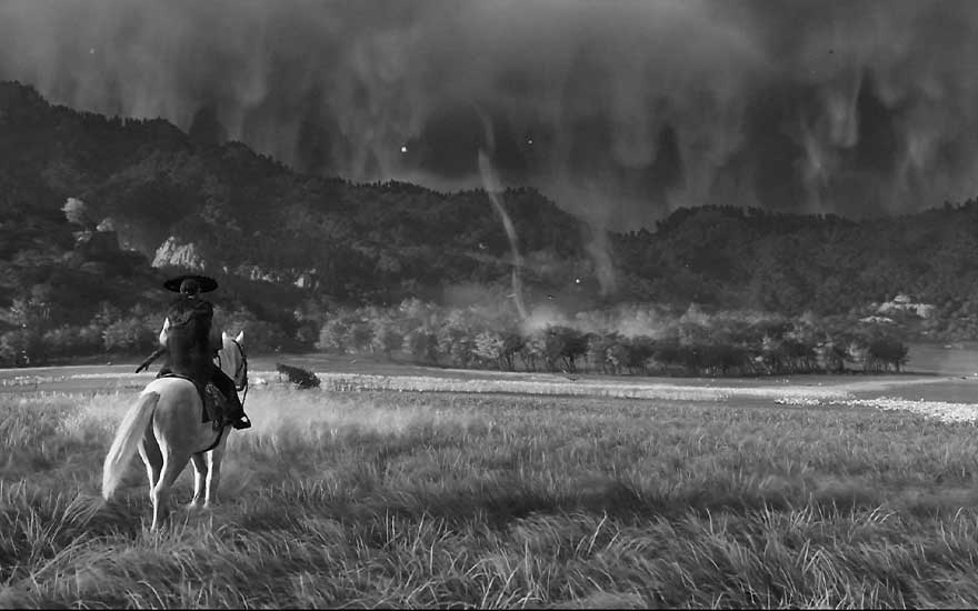 Image noir et blanc d'un cavalier à cheval dans une prairie avec des montagnes dramatiques en arrière-plan 