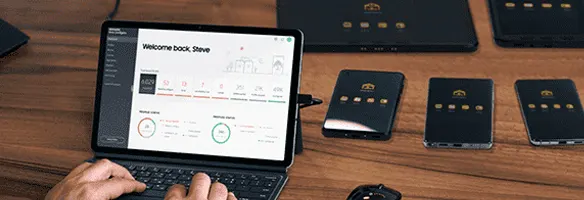 Een persoon typt op een laptop op een houten bureau. Verscheidene zwarte apparaten, elk met gouden accenten, staan op het bureau.