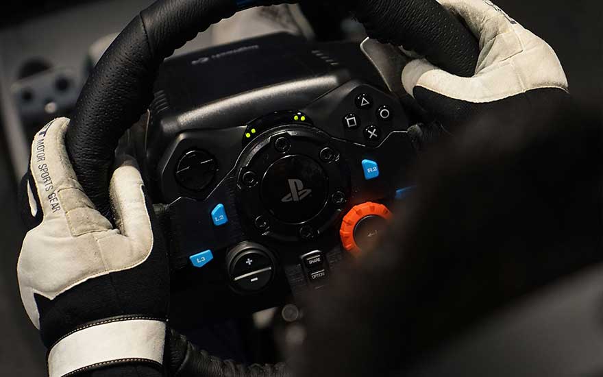 Gants blancs tenant un volant noir avec des boutons bleus, orange et noirs. Le volant a le logo Playstation au centre.