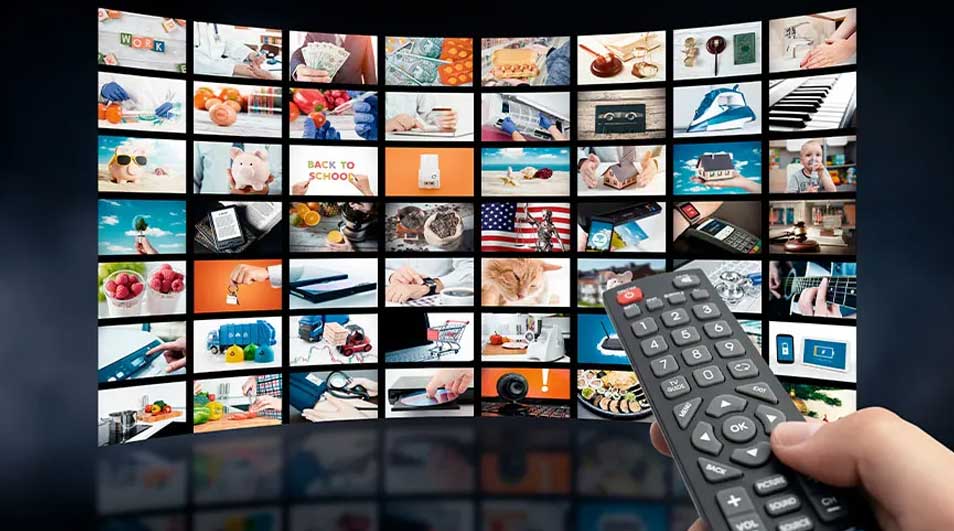 Mur d'écrans montrant diverses scènes, avec une main tenant une télécommande noire au premier plan.