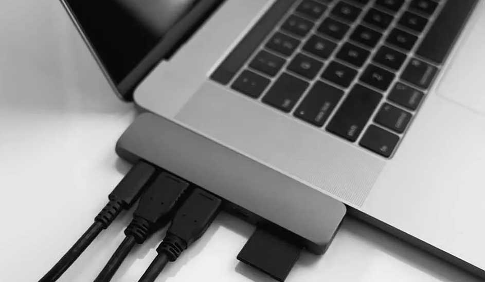 Gros plan d'un ordinateur portable gris avec des câbles noirs branchés sur un adaptateur gris sur une surface blanche.