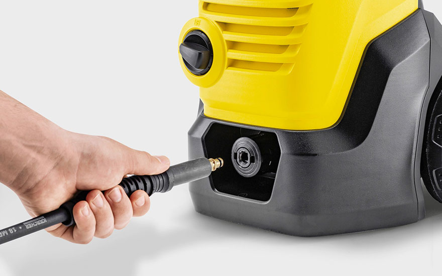 Une main connecte le tuyau noir à un nettoyeur haute pression jaune et noir, les points de connexion étant clairement visibles sur l'appareil.