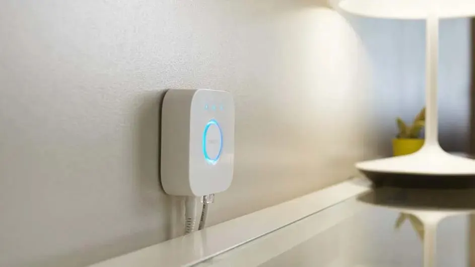 Un appareil blanc avec un anneau bleu est fixé à un mur beige près d'une lampe blanche sur une surface blanche.