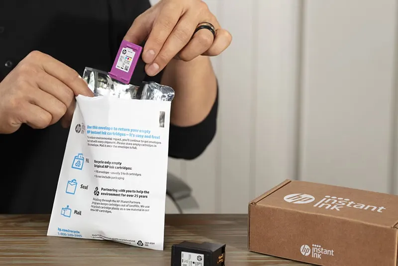 Hand plaatst een lege HP-inktcartridge in een retourenvelop naast een HP Instant Ink-doos.
