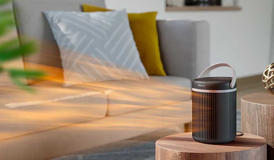 Lampe Philips noire sur table ronde en bois, canapé gris avec coussins en arrière-plan.