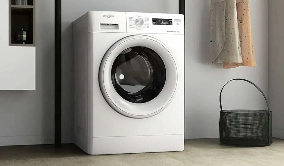 Een Whirlpool-wasmachine staat in een moderne wasruimte met een zwarte mand en hangende kleding. Het digitale display is duidelijk zichtbaar.