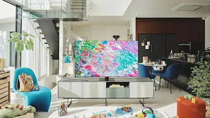 Een woonkamer met een grote tv op een dressoir, een blauwe stoel en een trap in de achtergrond.
