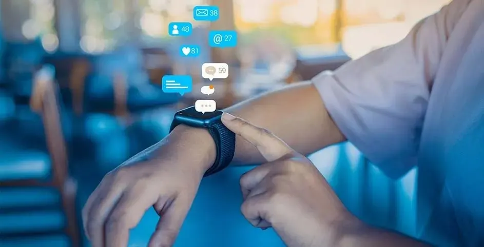 Zwarte smartwatch om een pols met meldingen. Een hand wijst naar het scherm, op een blauwe achtergrond.