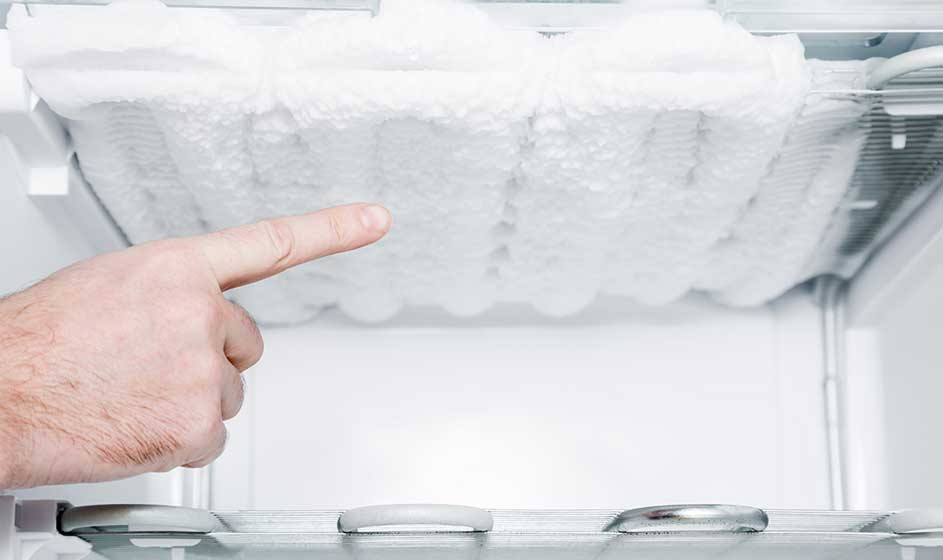 Une main montre une épaisse couche de glace et de givre accumulée dans un congélateur. L’espace intérieur semble presque entièrement obstrué.