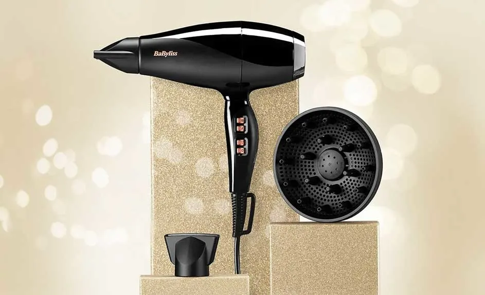 Zwarte BaByliss haardroger met opzetstukken op goudkleurige blokken tegen een beige achtergrond.