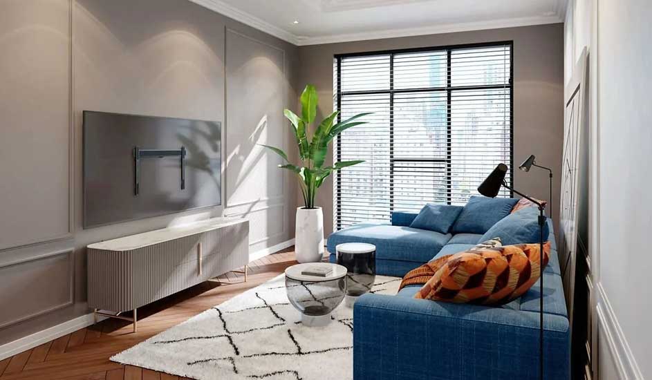 A modern living room with a blue corner sofa, large plant, rug and an empty wall bracket for a TV. No brand is visible.