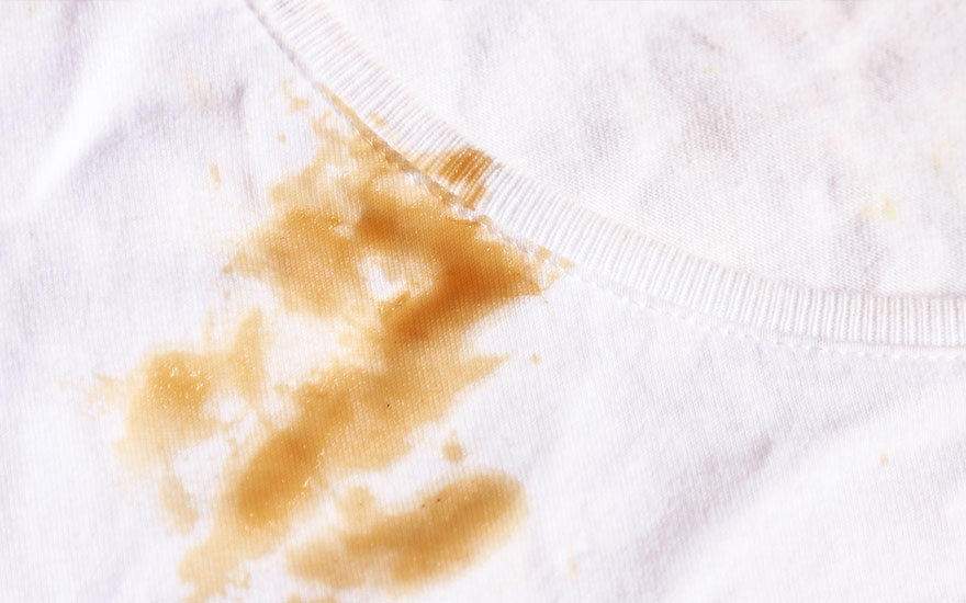 Un t-shirt blanc avec une tache brune près de l'encolure. Le tissu est froissé et la tache semble humide.