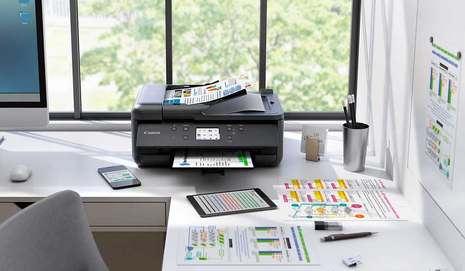 Een printer op een bureau met een telefoon, tablet, papier en een computer tegen een raam.