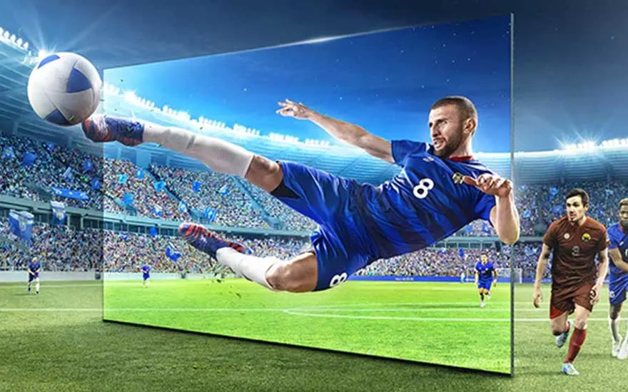 Een grote tv toont een spannende voetbalwedstrijd, met een speler in blauwe uitrusting die naar de bal schiet in een vol stadion.