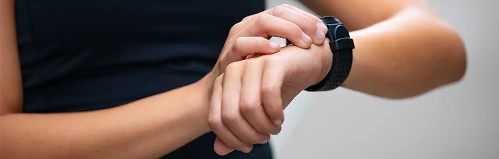 Quelqu’un règle ou consulte une montre connectée noire à son poignet, avec les mains nettes sur un fond neutre.