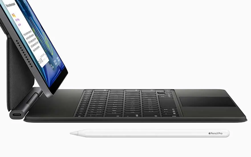 Une vue latérale montre un iPad sombre sur un clavier noir avec charnière, grand pavé tactile et Apple Pencil blanc devant.