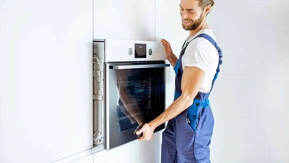 A white oven is being installed into a white cabinet. The oven has a glass door and silver handle. The wall is white.