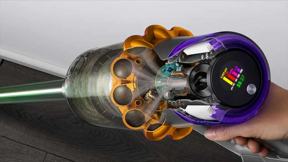 Un aspirateur sans fil violet et or est tenu à la main. Un écran affiche des données et une lumière verte brille par le tube.