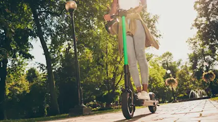 Une trottinette verte sur une allée pavée dans un parc. Arbres et lampadaire en arrière-plan.
