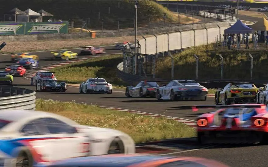 Vue d'une course automobile avec diverses voitures colorées sur une piste entourée de verdure et de spectateurs.
